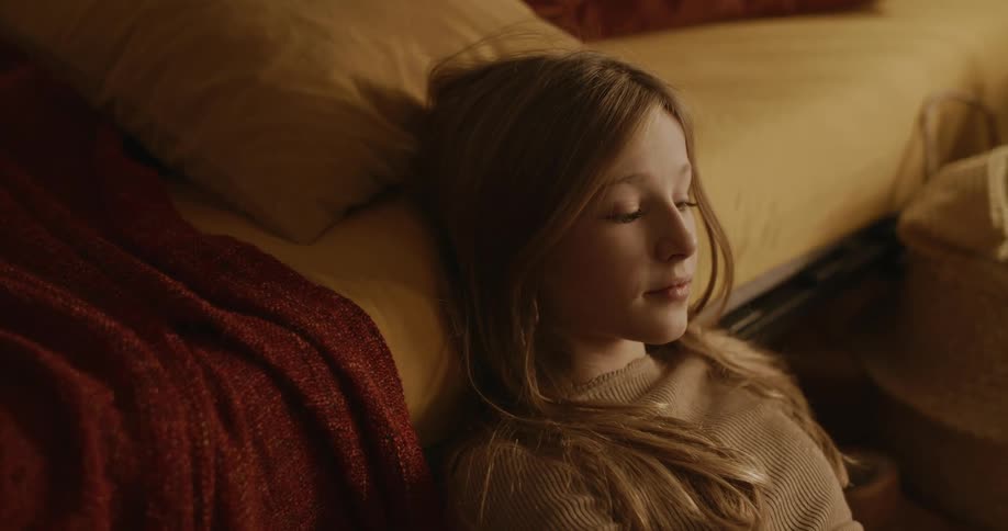 Portrait of a young teenage girl sitting on the floor next to the bed giving a slight smile