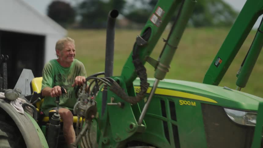 A farmer driving a green bulldozer picks up hay bales