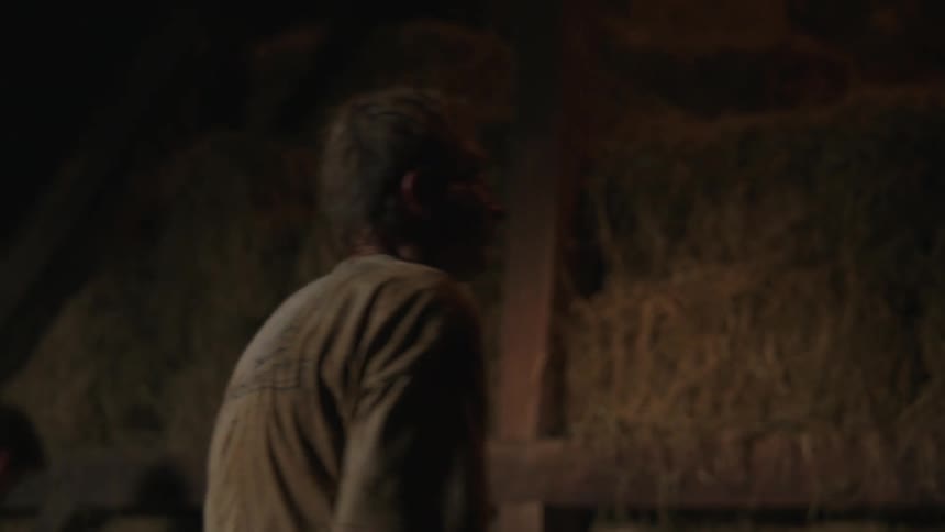 Two farmhands work together to stack bales of hay in a barn