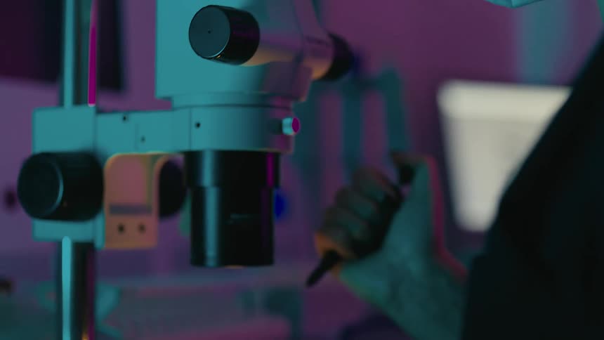 Woman in the laboratory applying a needle and looking at a small vessel under the microscope