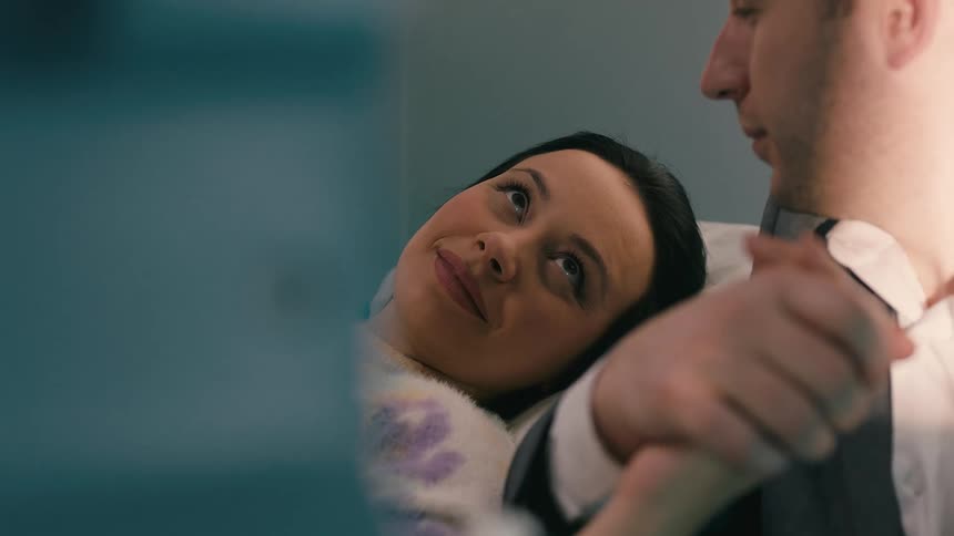 Man holds the hand of a lady laying on the bed indoor while looking in her eyes