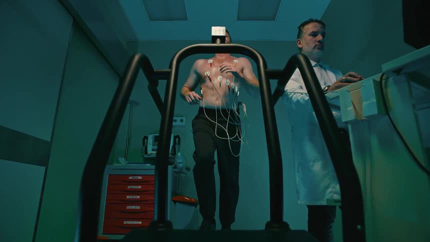 A person is undergoing a stress test on a treadmill monitored by a healthcare professional
