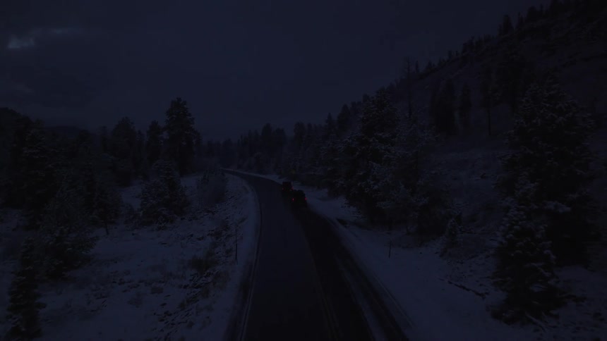 Aerial view of a vehicle driving on a road through a snowy landscape at night
