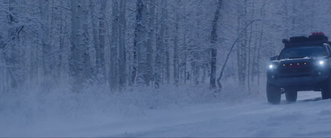 A snowy landscape with two offroad vehicles on a path surrounded by trees
