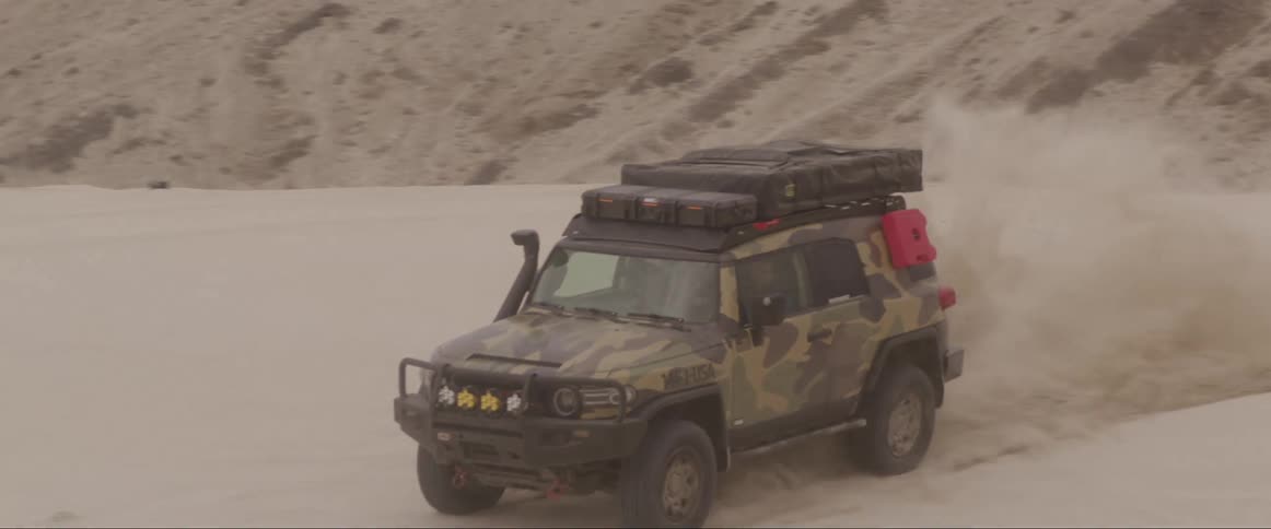 Vehicle with air intake speeds across sand near mountains