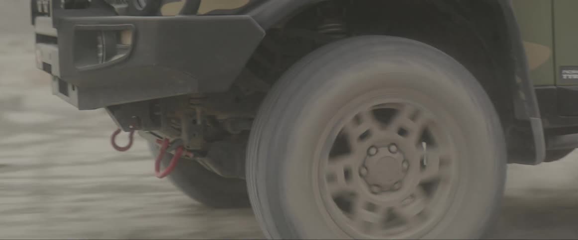 An atv with camouflage paint driving across a dirt road