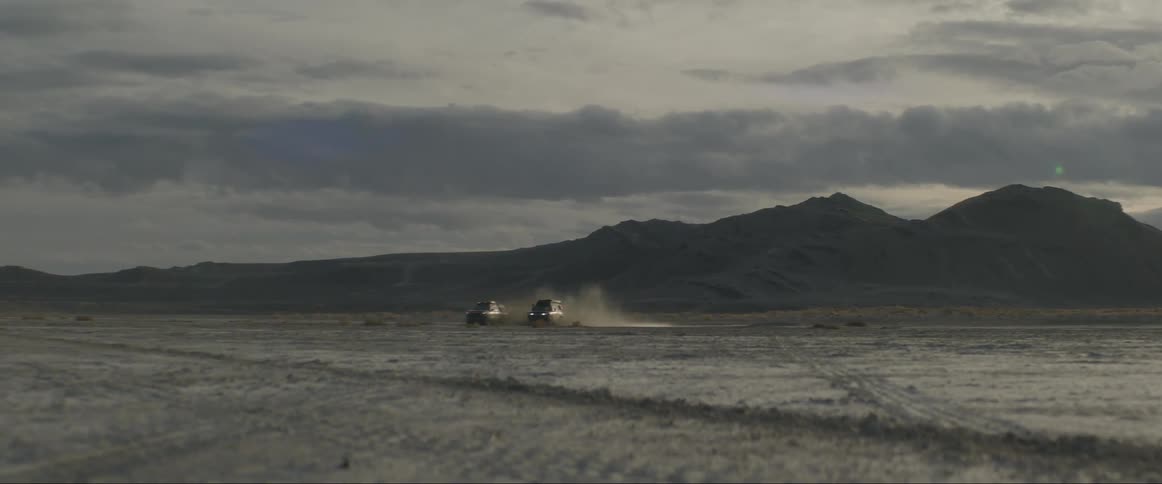 Two vehicles race each other across a desert plain