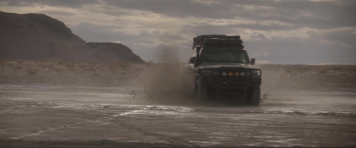 An off road vehicle driving at high speed across a barren landscape splashes water