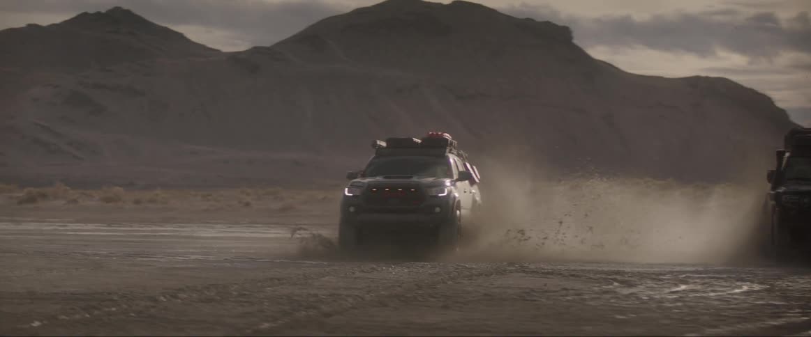 Two vehicles splashes water while speeding on a sandy road at midday