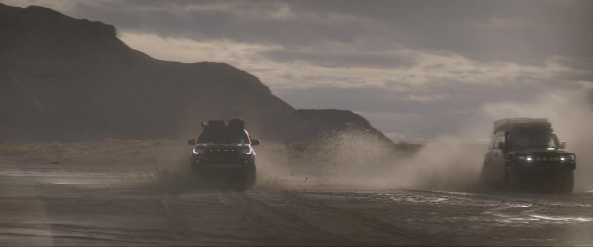 Vehicles splashes water while running on a sandy road at sunset
