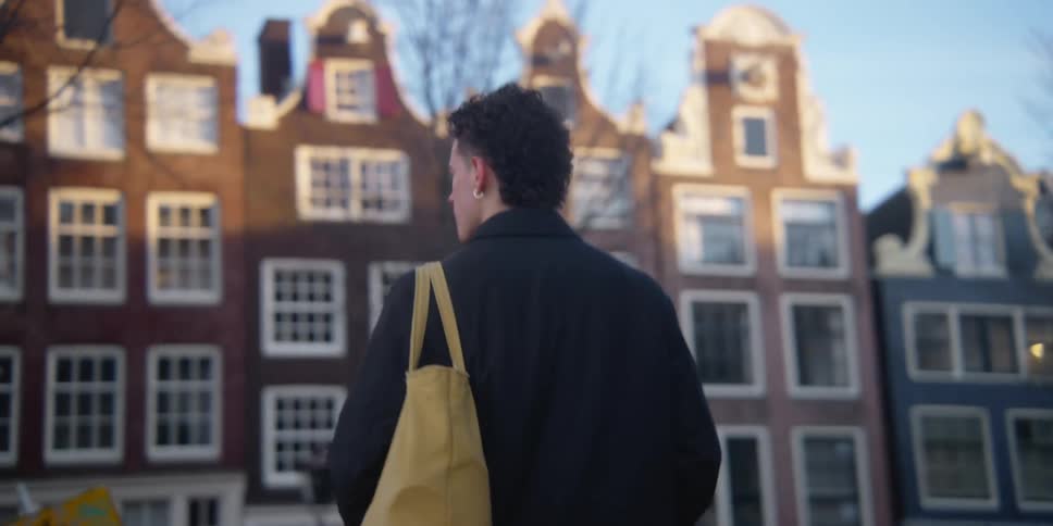 Back of a man walking towards a building while carrying a side bag at daytime