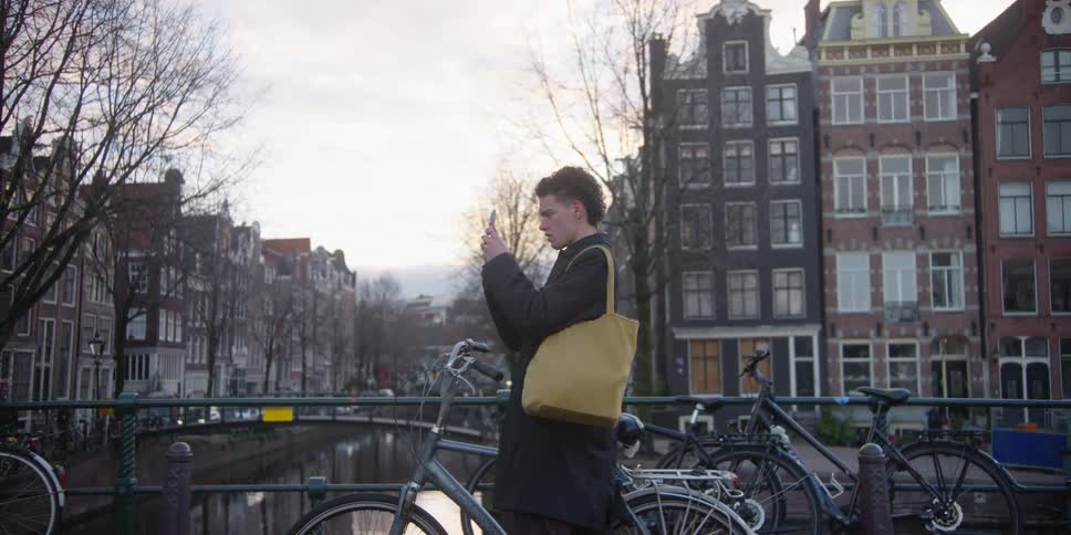 A young man riding a bicycle in amsterdam stops to record a video with his phone
