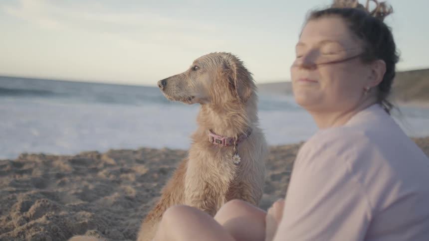 Young woman sitting on the beach sand next to her dog
