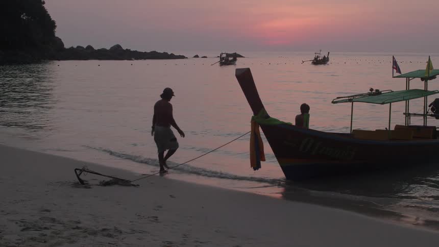 A man hooks a boat to the sand while docking at sunset