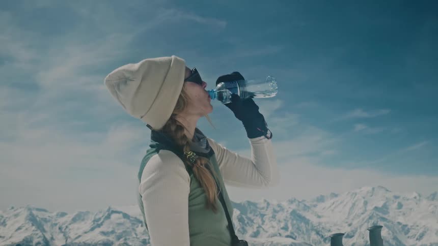 Lady drinks water while standing on a mountain at midday