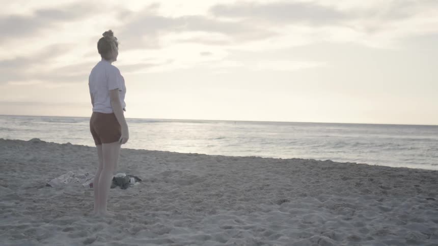 Young adult female playing fetch with two dogs on a beach beside the ocean on a cloudy day