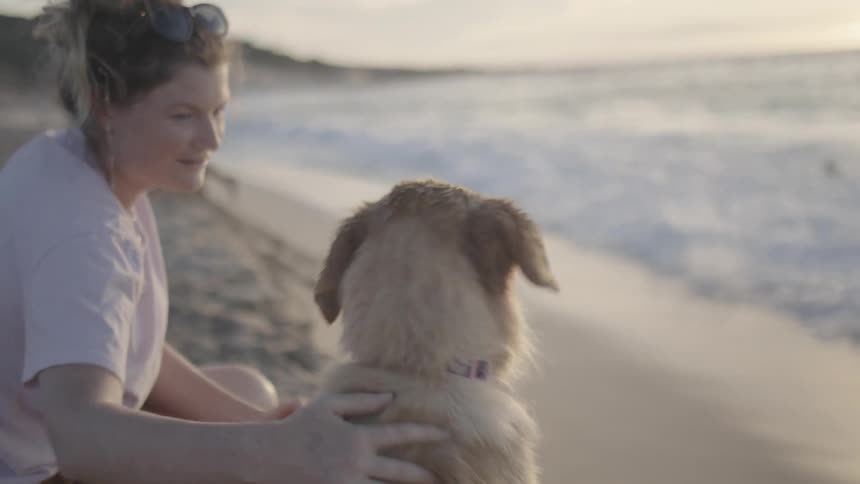 Lady rubs the head of her dog while at the beach side during the day