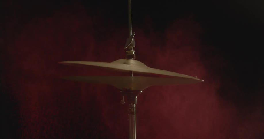 A drummer strikes a hi-hat cymbal scattering pink powder