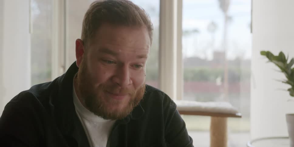 A man sitting in a house speaks and gestures with his hands
