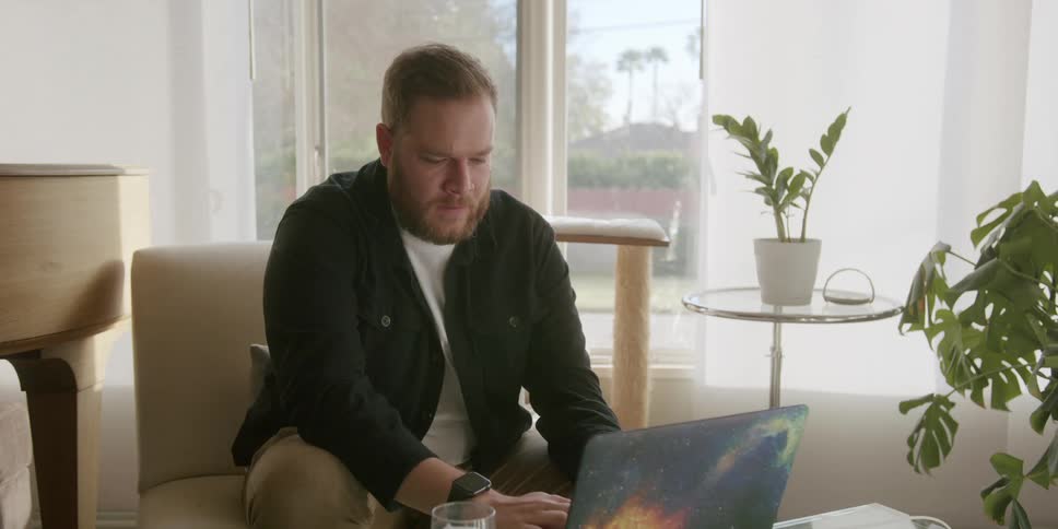 Man sitting in an armchair working on the laptop and with a worried facial expression