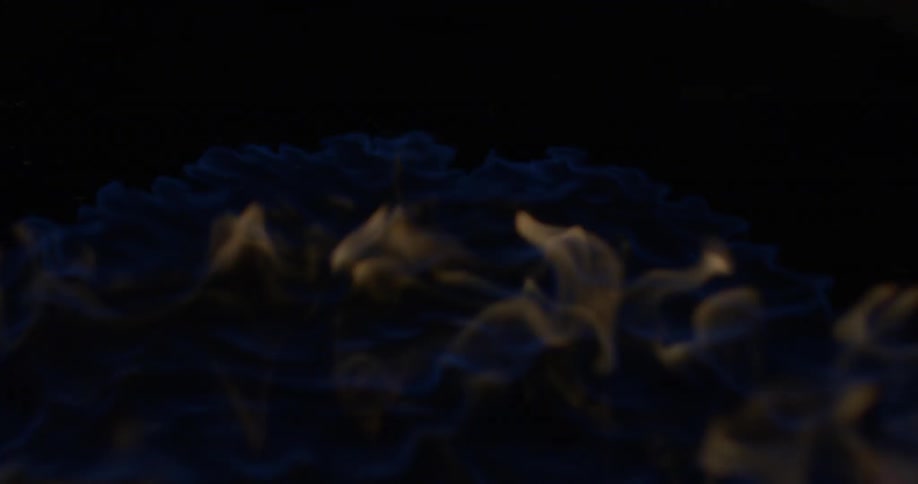 A blue and orange flame spreads and swirls as it burns
