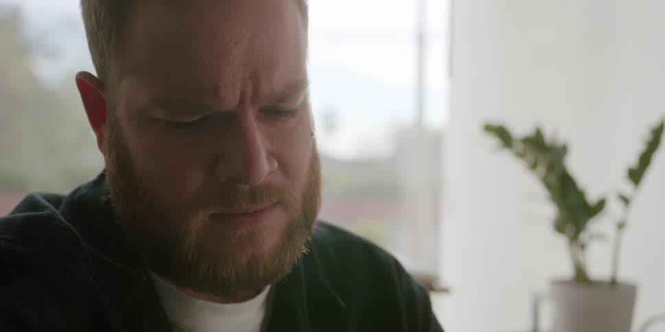 A man in a room looks sad in silence while frowning then talks into his smart watch