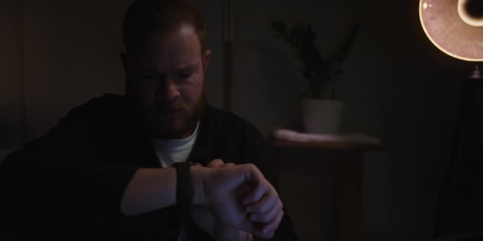 A man sitting in a room at night checking his watch