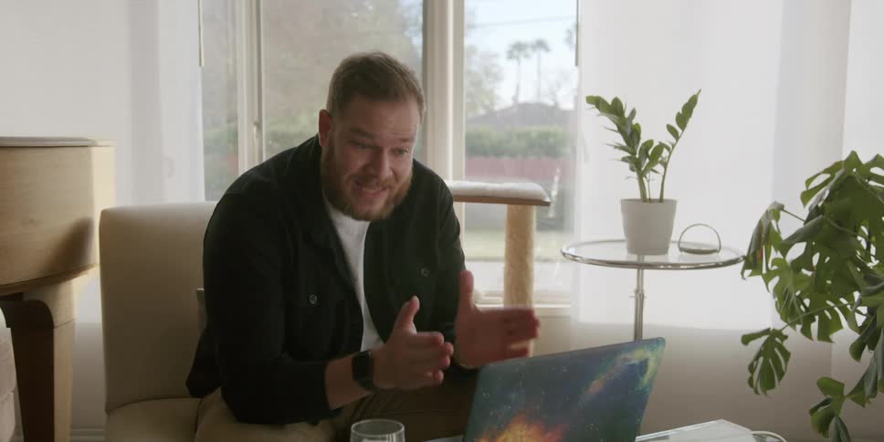 A man sitting in a room talking to others on a laptop