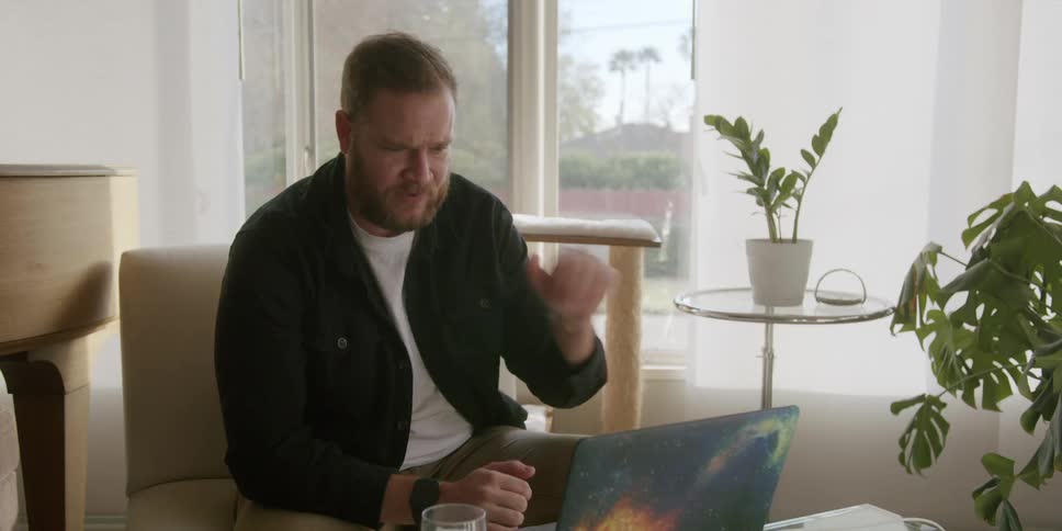 Man sitting in an armchair having a conversation on a laptop in an indoor setting