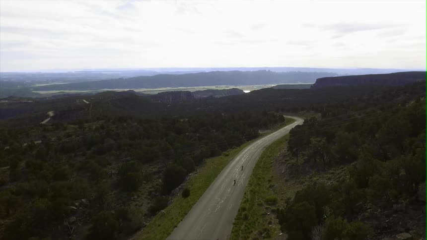 Two skateboarders ride down a mountain road