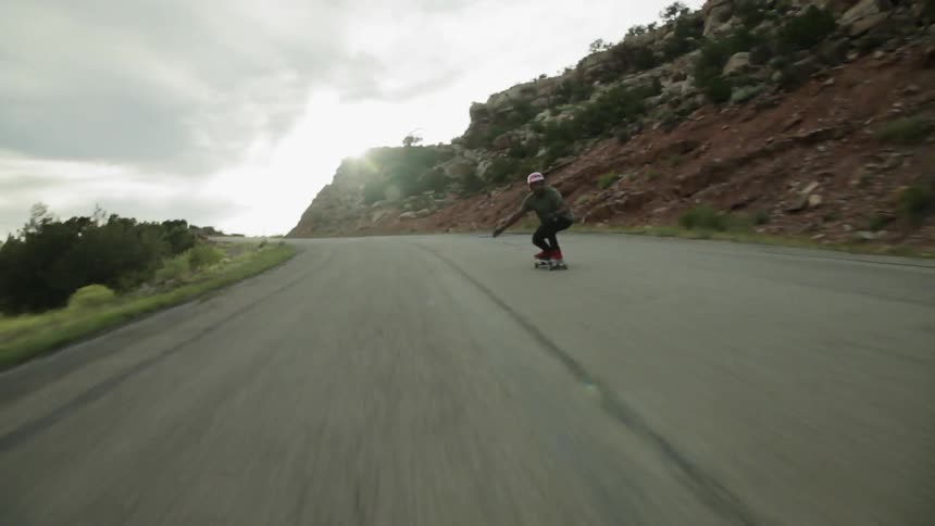 A skateboarder rides down a mountain road at a fast speed
