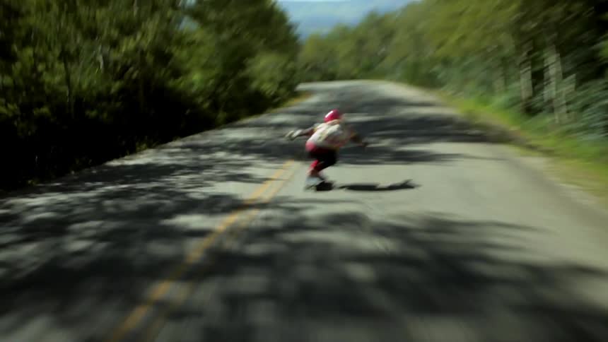 A skateboarder speeds down a tree-lined road