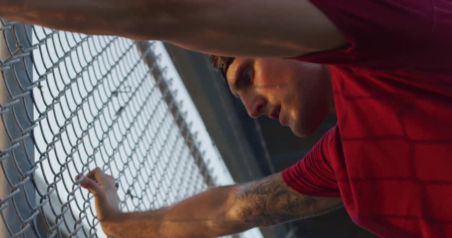 A tired man in sportwear leaning against a metal fence