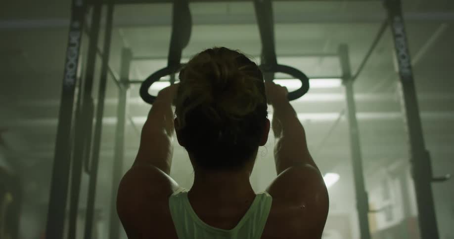 A woman in a gym pulls herself up with metal rings