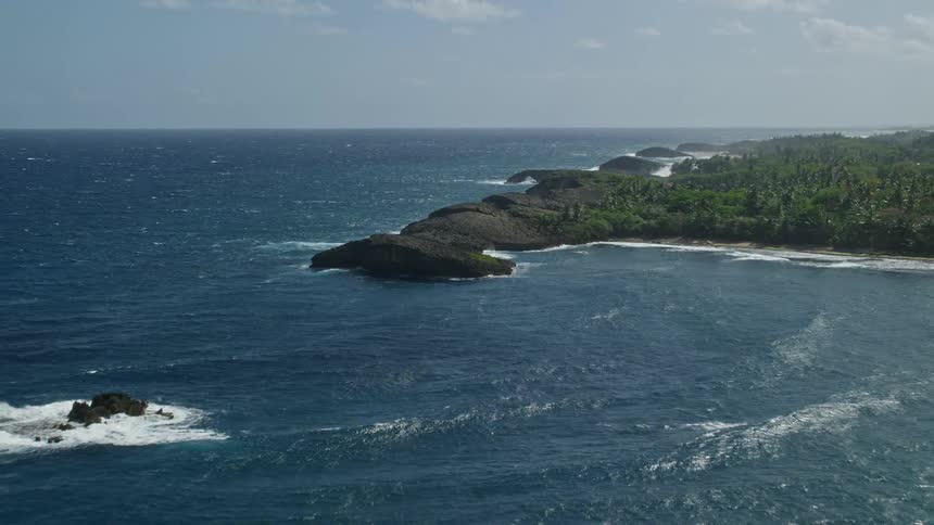 A rocky and green coastline next to the ocean under a blue sky