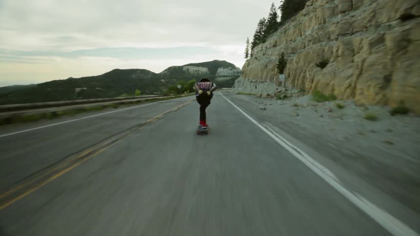 A skateboarder speeds down a mountain road