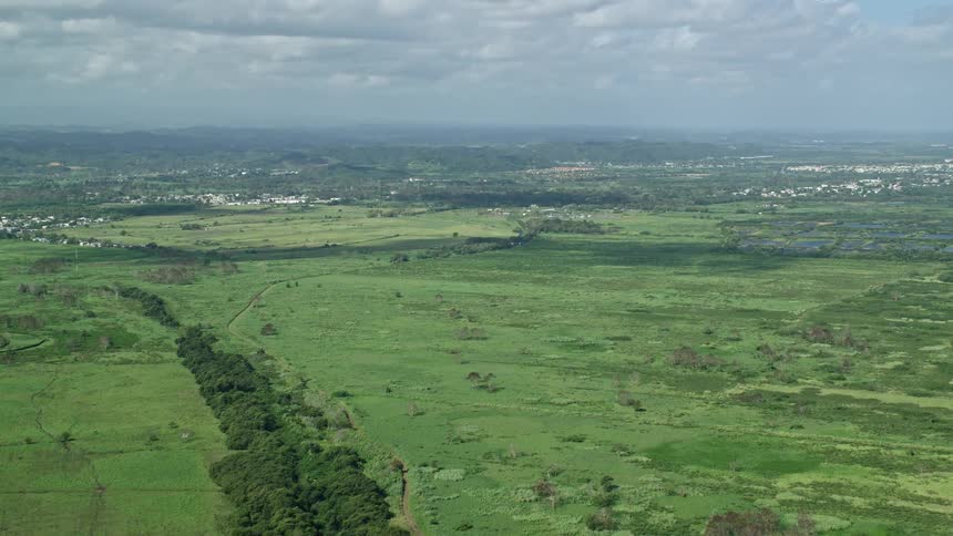 A rural area with a huge field of green grass and in the background there is a town of small houses