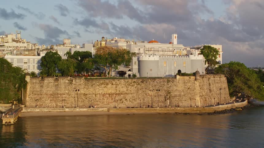 A large building of ancient architecture all white on top of a large wall facing the sea