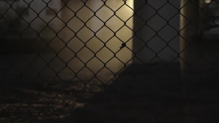 Sunlight shines through dust behind a chain link fence