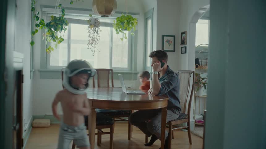A father sits in the kitchen while his sons play energetically