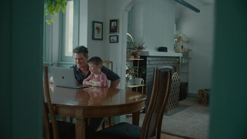 Father sitting at the table with his son and both watching something on a laptop