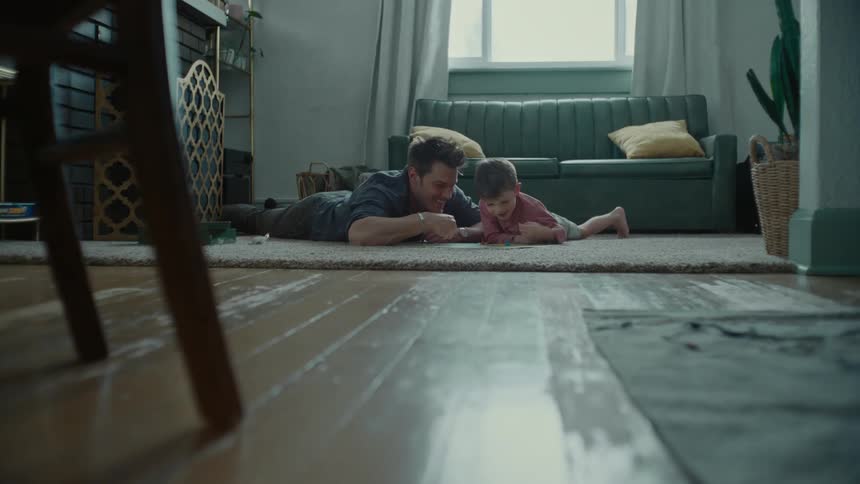 Father lying on the carpet with his little son both playing a board game smiling