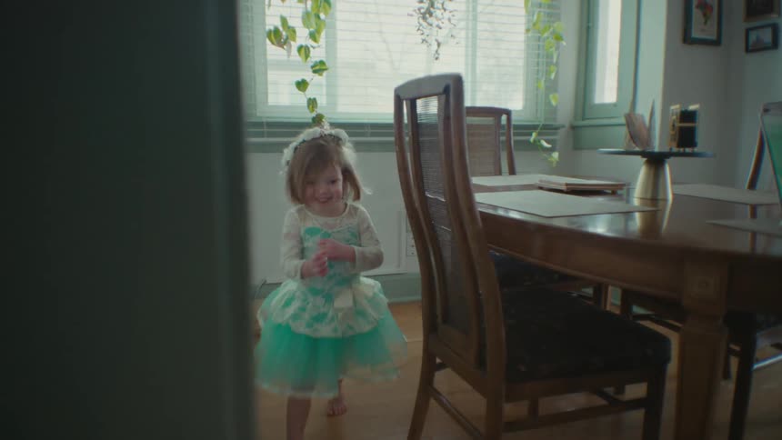 Little girl running in circles in the room while her mother sits at the table on the laptop