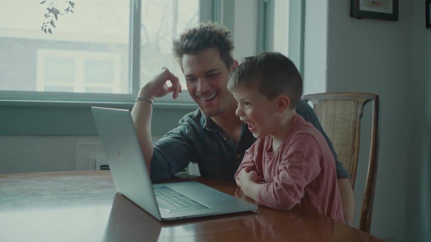 A father smiles as he look at the screen of a laptop with his young son