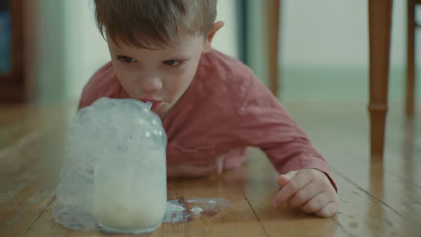 A little boy blows bubbles with milk