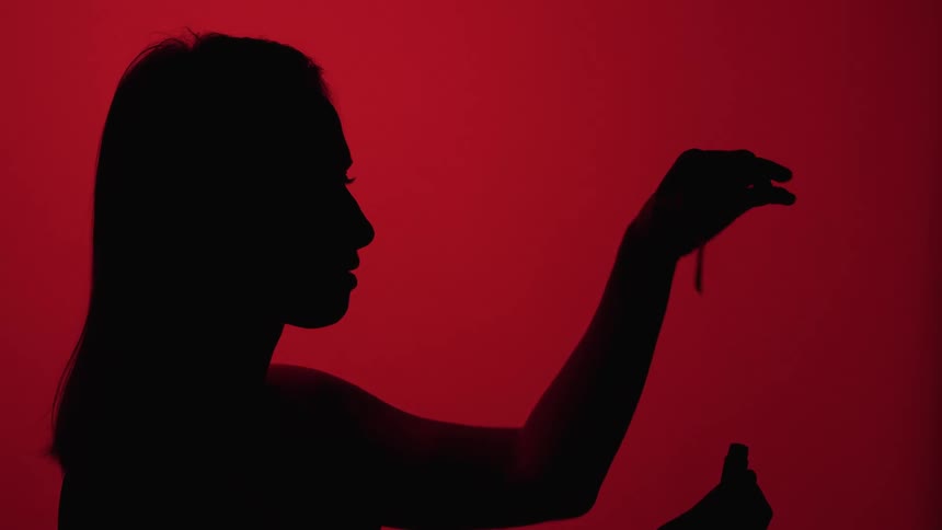 Woman silhouetted against red background removes top from bottle of makeup
