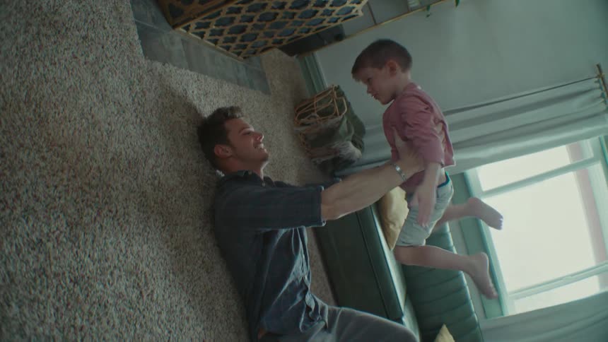 A man is lying on the floor holding his young son above him playing airplane