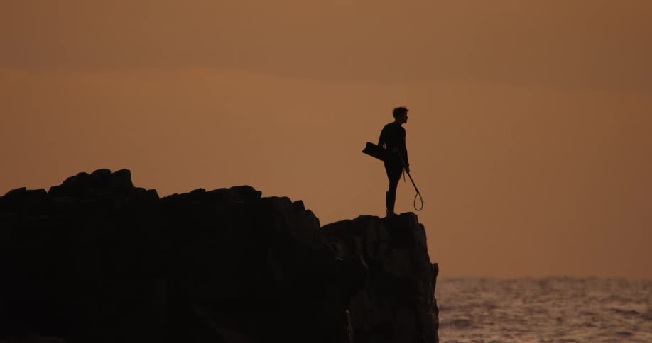 Silhouette of a man on a cliff facing the sea with a reddish sky