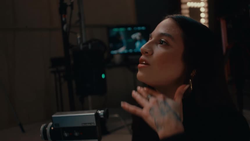 Portrait of a woman holding a professional camera inside a studio and talking to someone