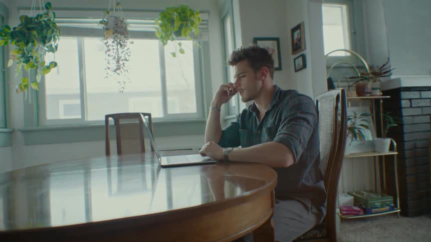 A child runs by a man sitting at a table and talking on a phone